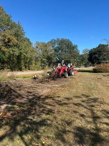 Red tractor clearing debris on a grassy field under a bright blue sky.