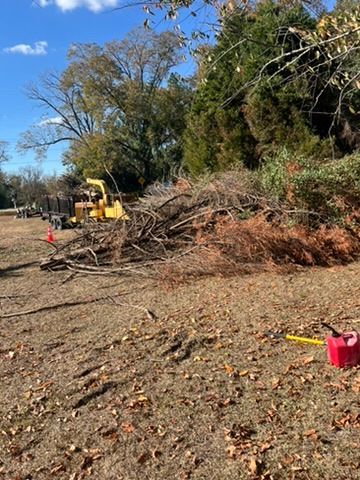 A pile of branches next to a yellow wood chipper on a grassy area, a red gas can.