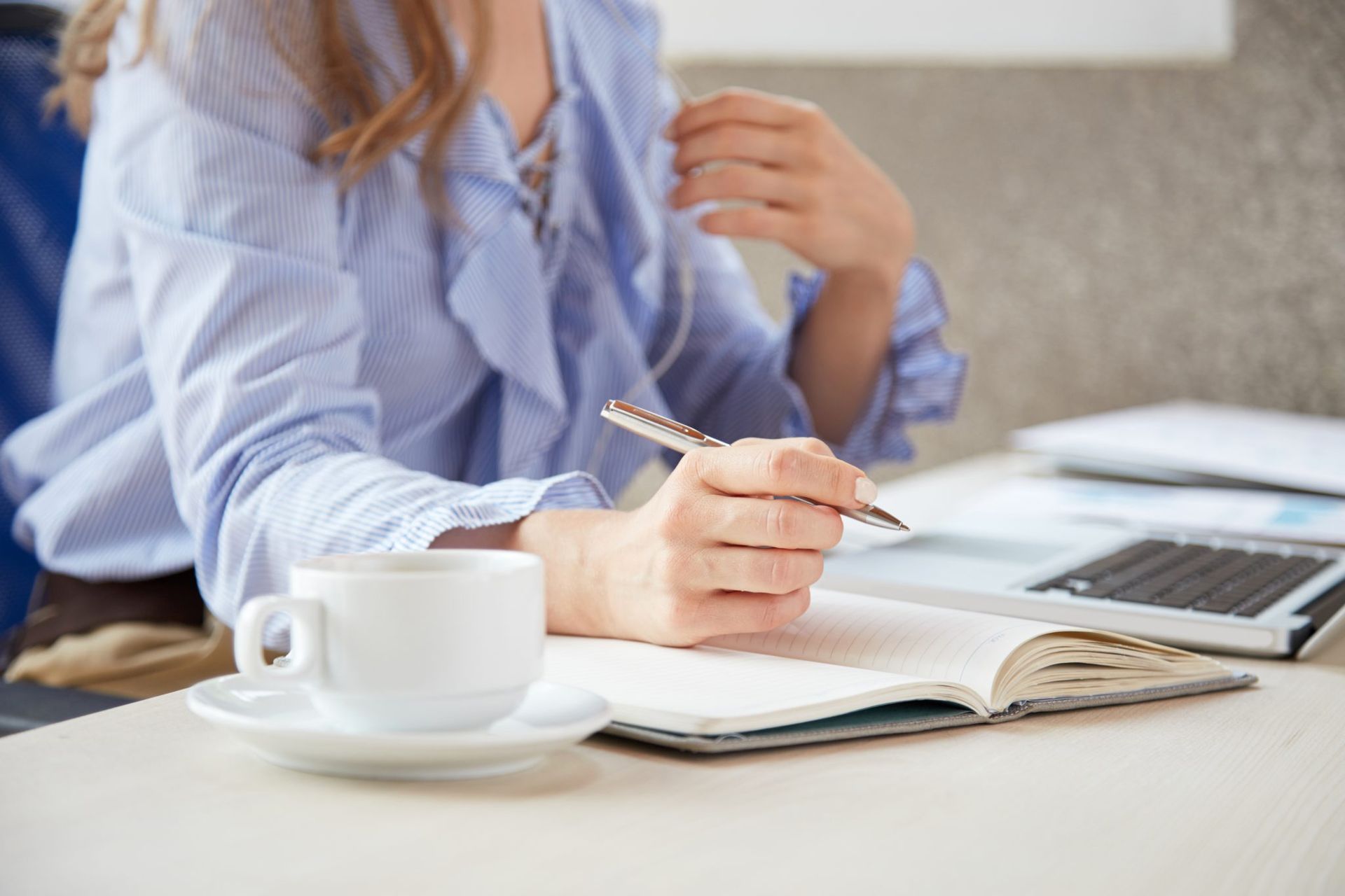 Una mujer está sentada en una mesa con una taza de café y un cuaderno.