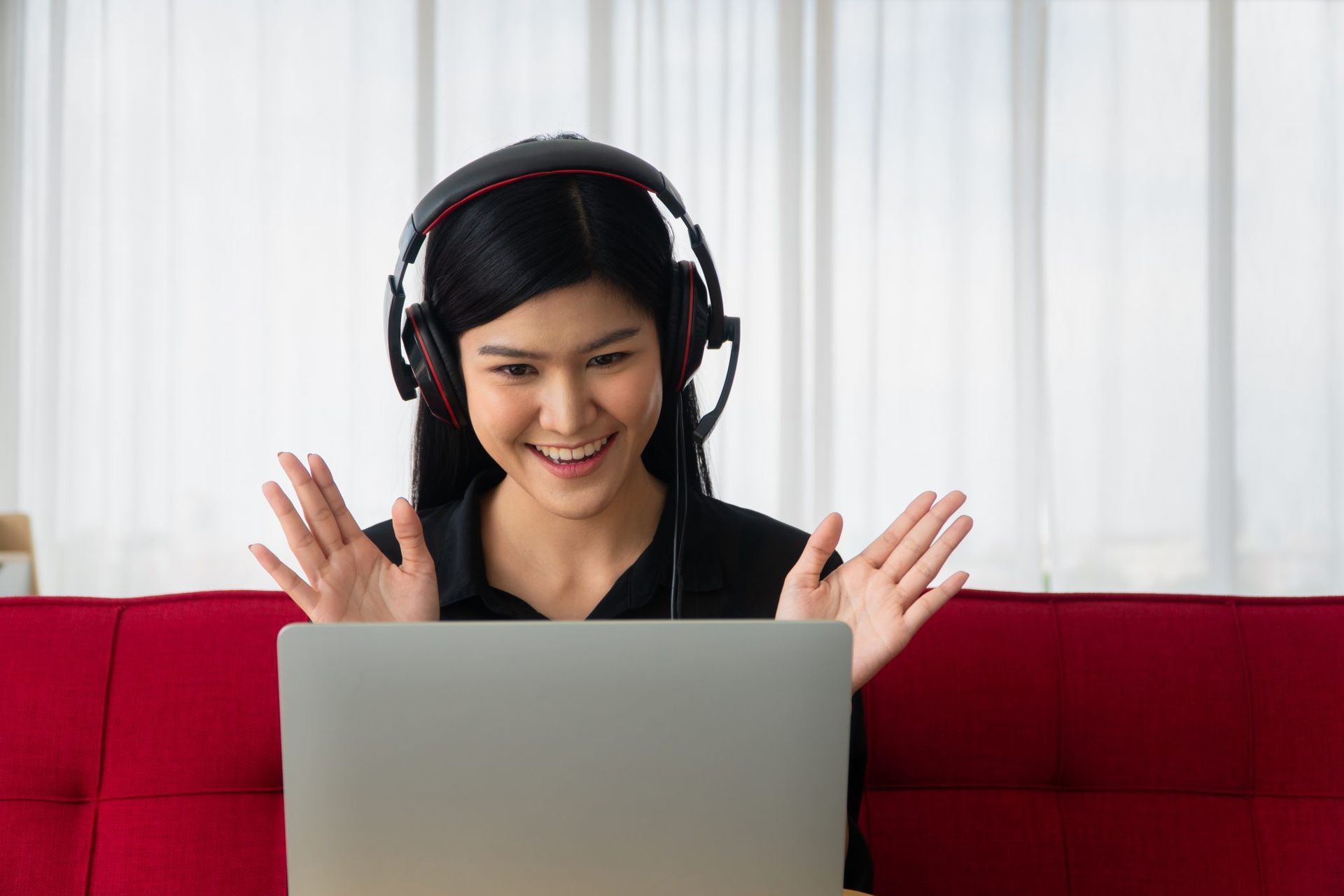 Una mujer con auriculares está sentada en un sofá utilizando una computadora portátil.