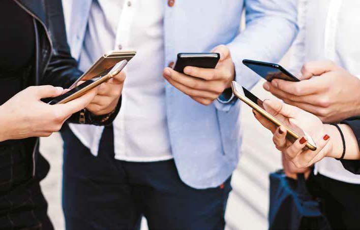 Un grupo de personas están paradas una al lado de la otra mirando sus teléfonos.