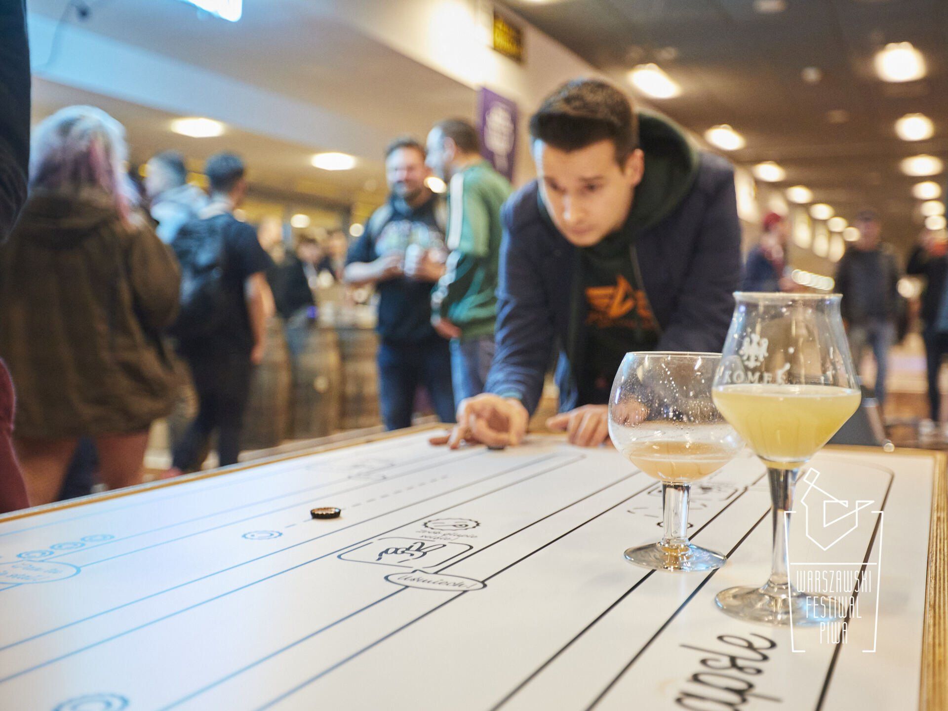 mężczyzna gra w grę ze szklanką piwa na stole.