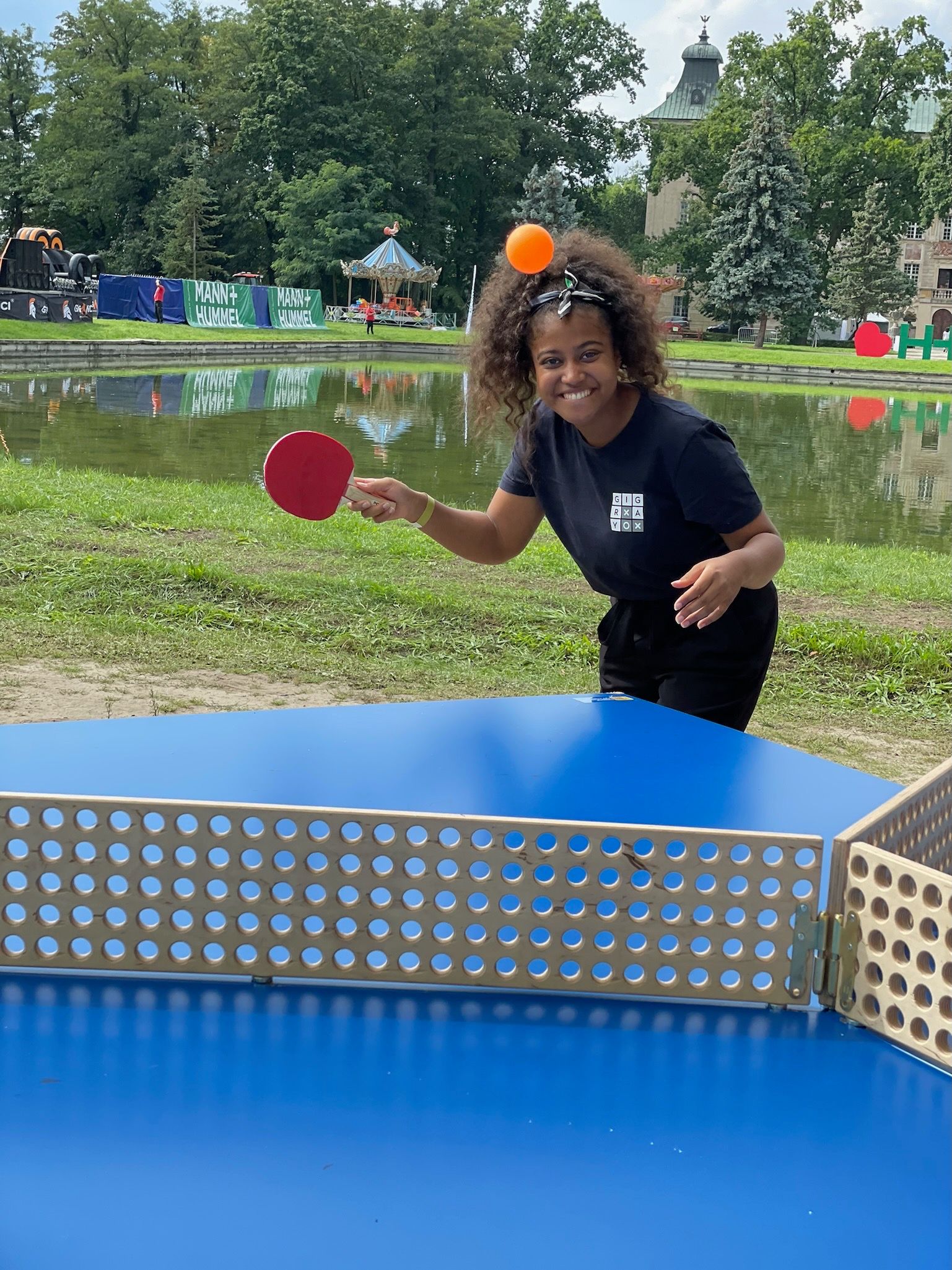 kobieta gra w ping-ponga na niebieskim stole w parku.