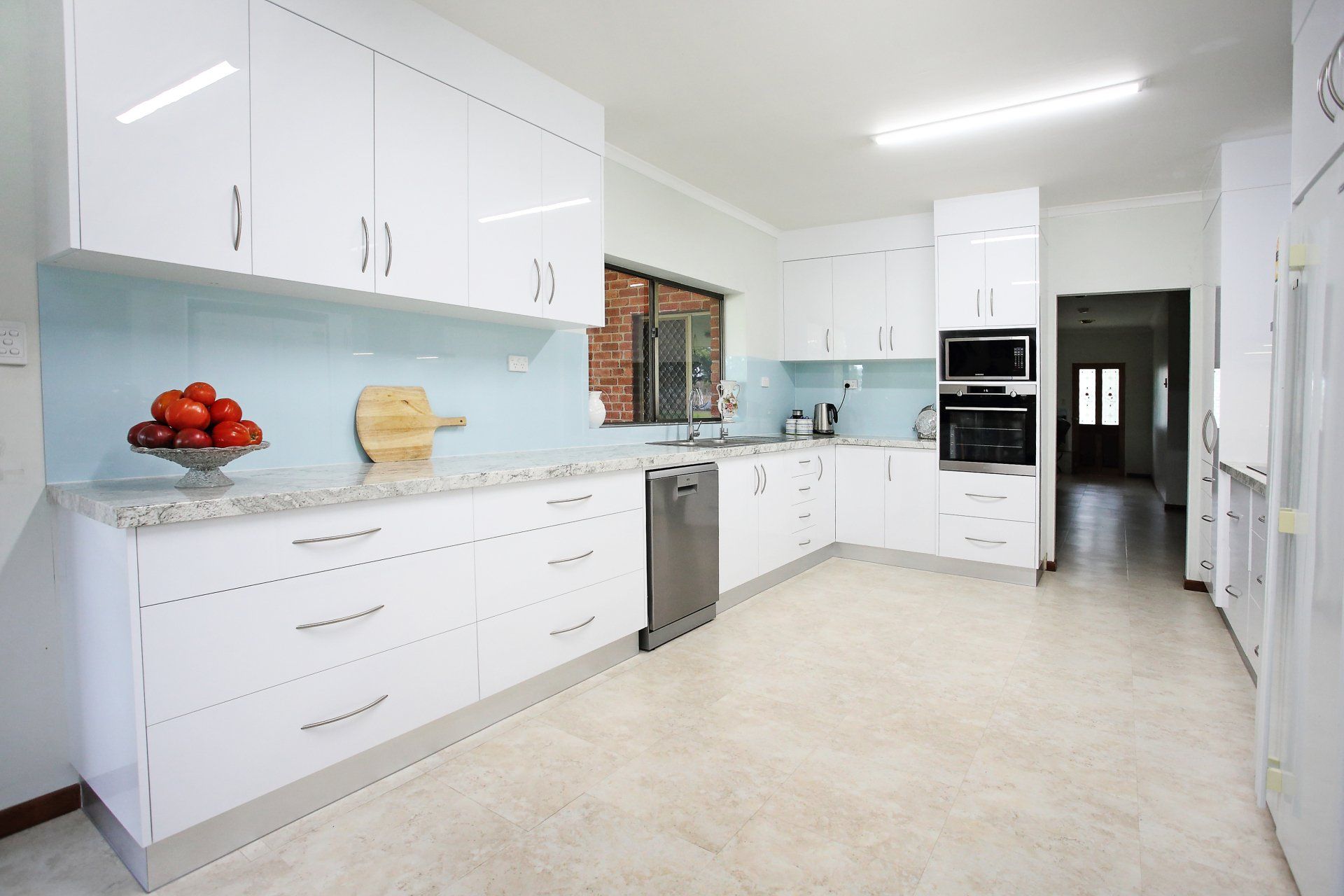 A kitchen with white cabinets and a bowl of tomatoes on the counter