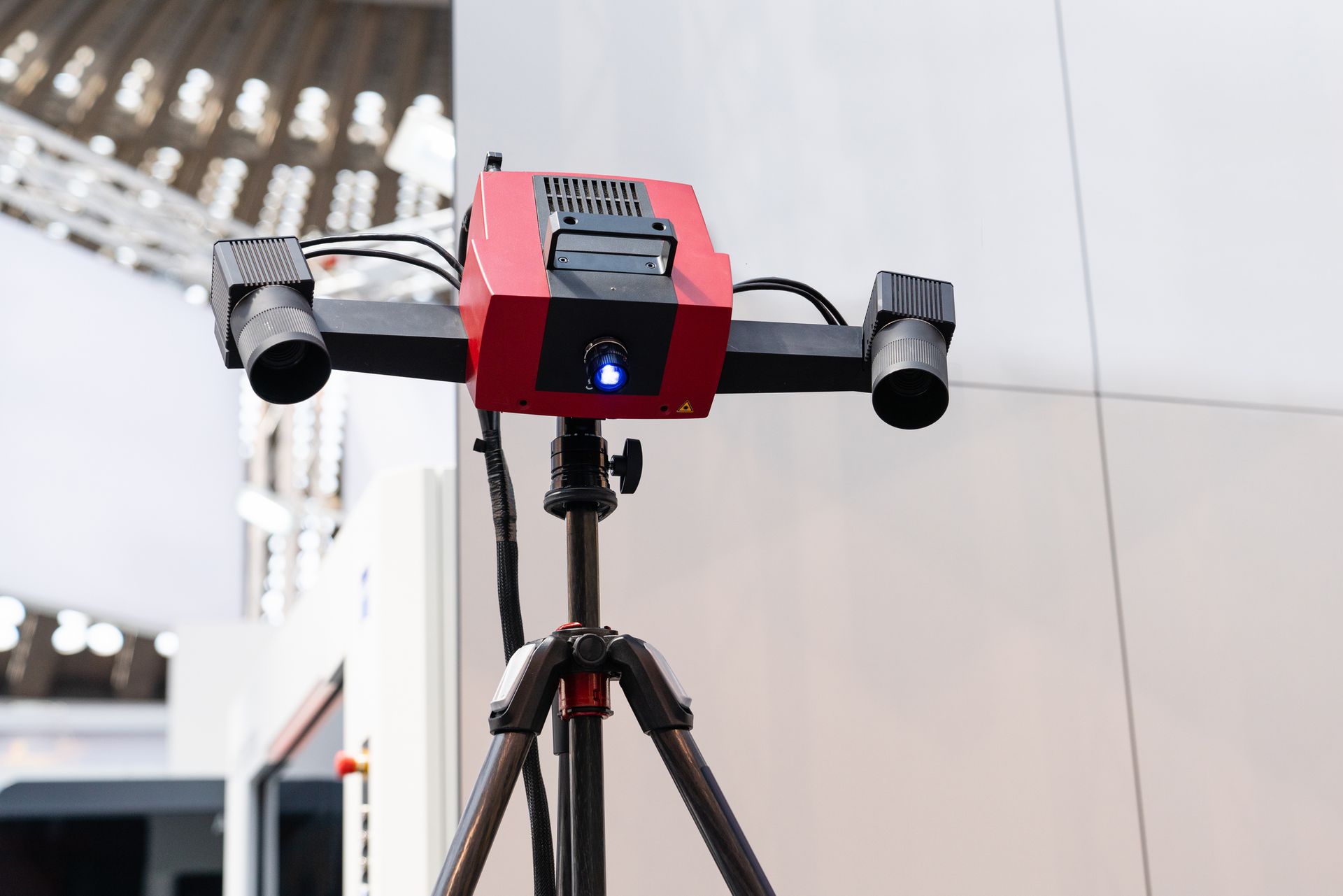 Wide view Image of a red 3D scanner on a tripod.]