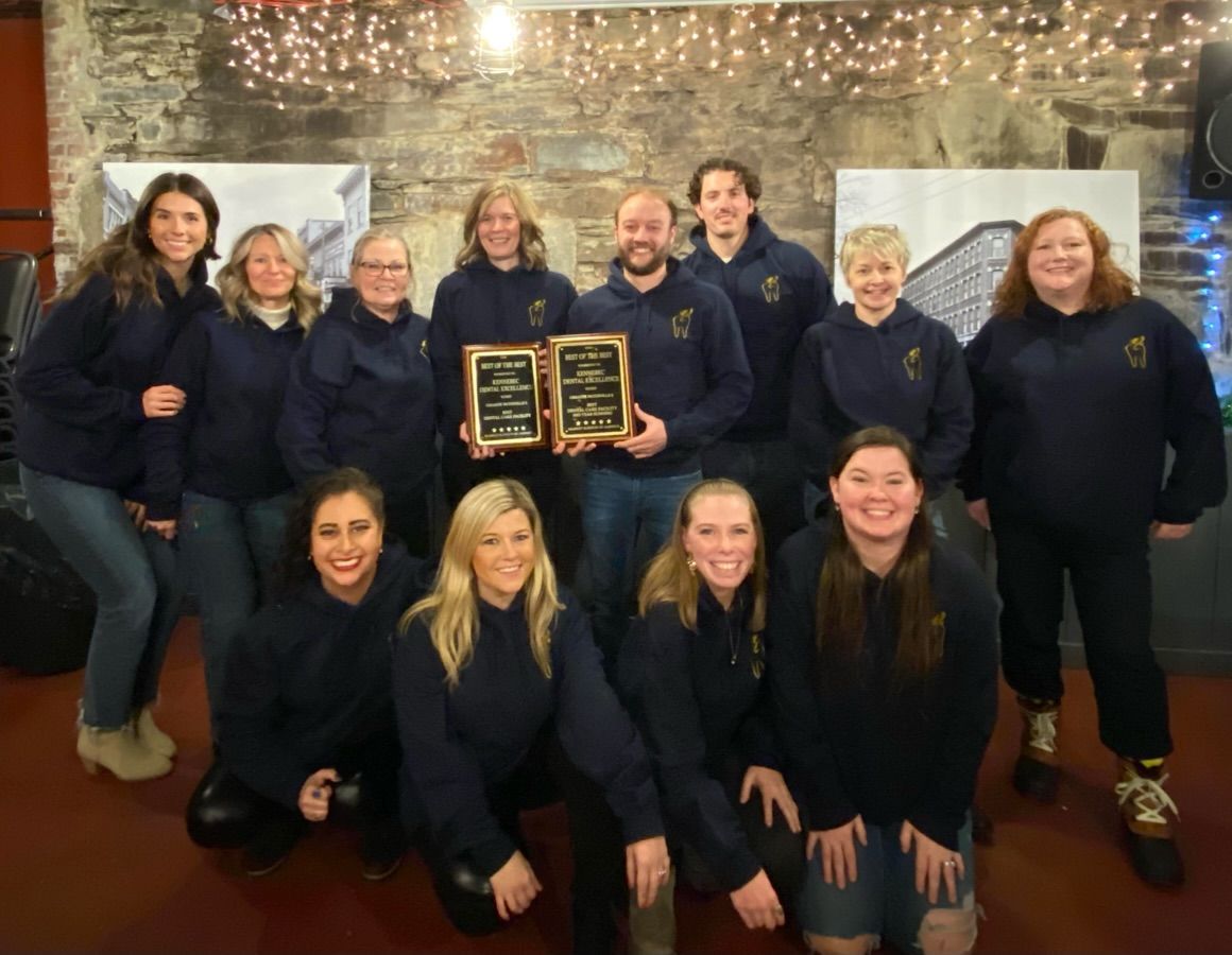 Woman smiling at mirror during a dental exam; dentist pointing at her cheek.
