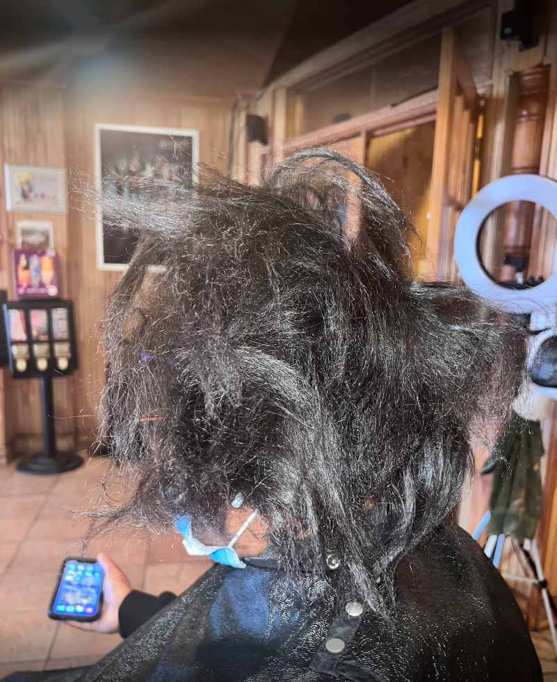 A woman is getting her hair cut in a salon while holding a cell phone.