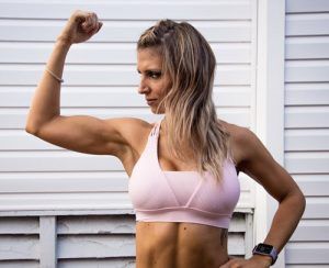 A woman in a pink sports bra is flexing her muscles.