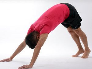 A man in a red shirt and black shorts is doing a yoga pose