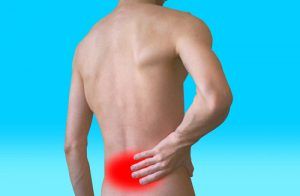 A shirtless man is holding his back in pain.