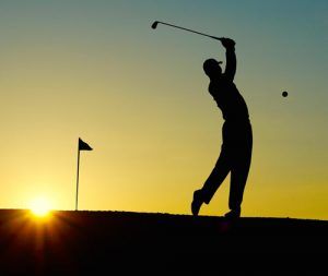 A silhouette of a man swinging a golf club at sunset