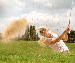 A woman is hitting a golf ball out of a bunker on a golf course.
