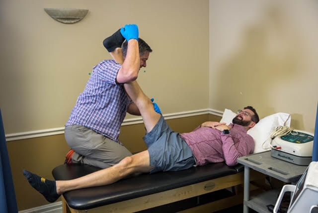 A man is laying on a table while a doctor stretches his leg.