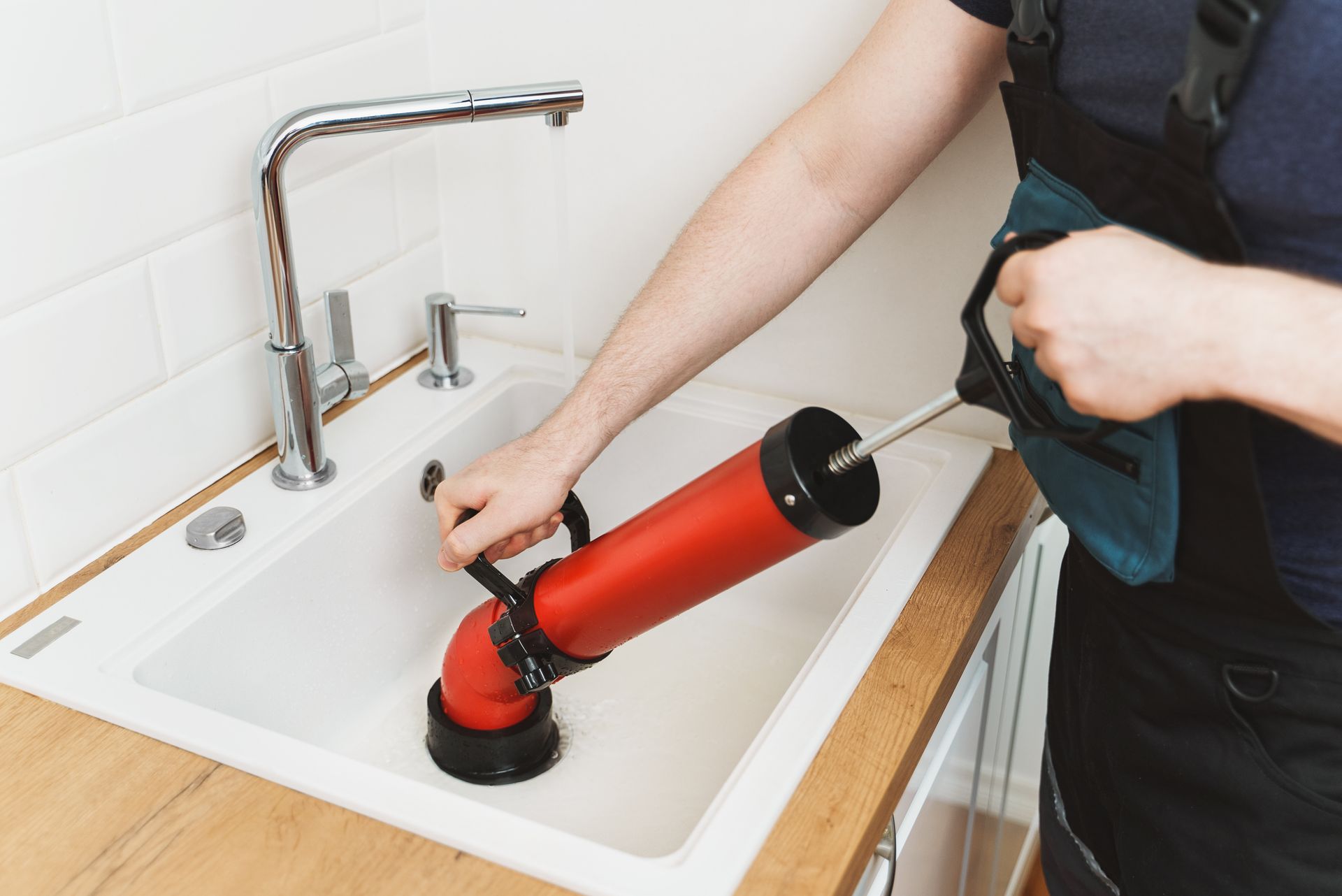 A plumber unclogging a kitchen sink with a professional force-pump cleaner.