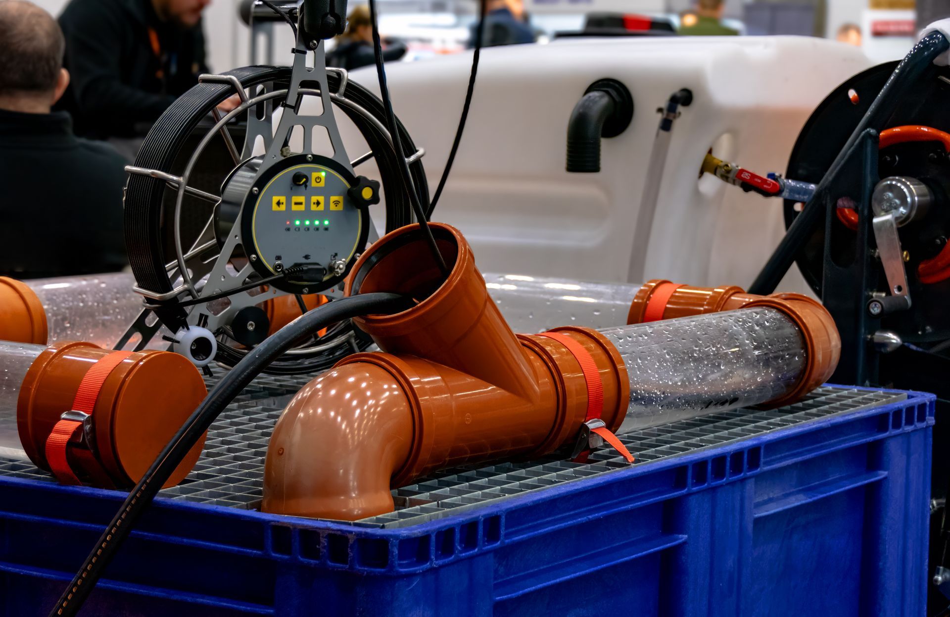 Camera for inspecting pipes with brown and transparent plastic pipe sections on blue crate.