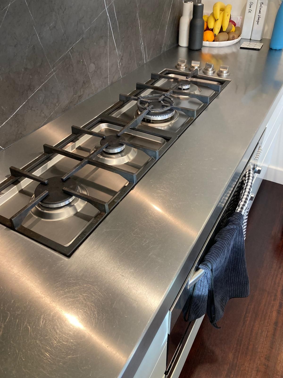 Person wearing orange gloves using a wrench to tighten a gas line under a stovetop.