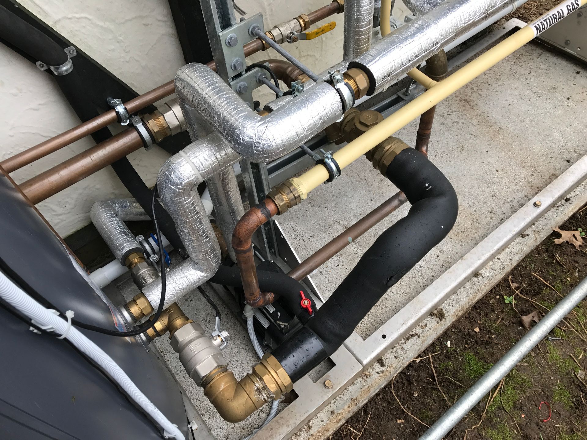 A person wearing red gloves inspects pipes with a device inside a utility room.