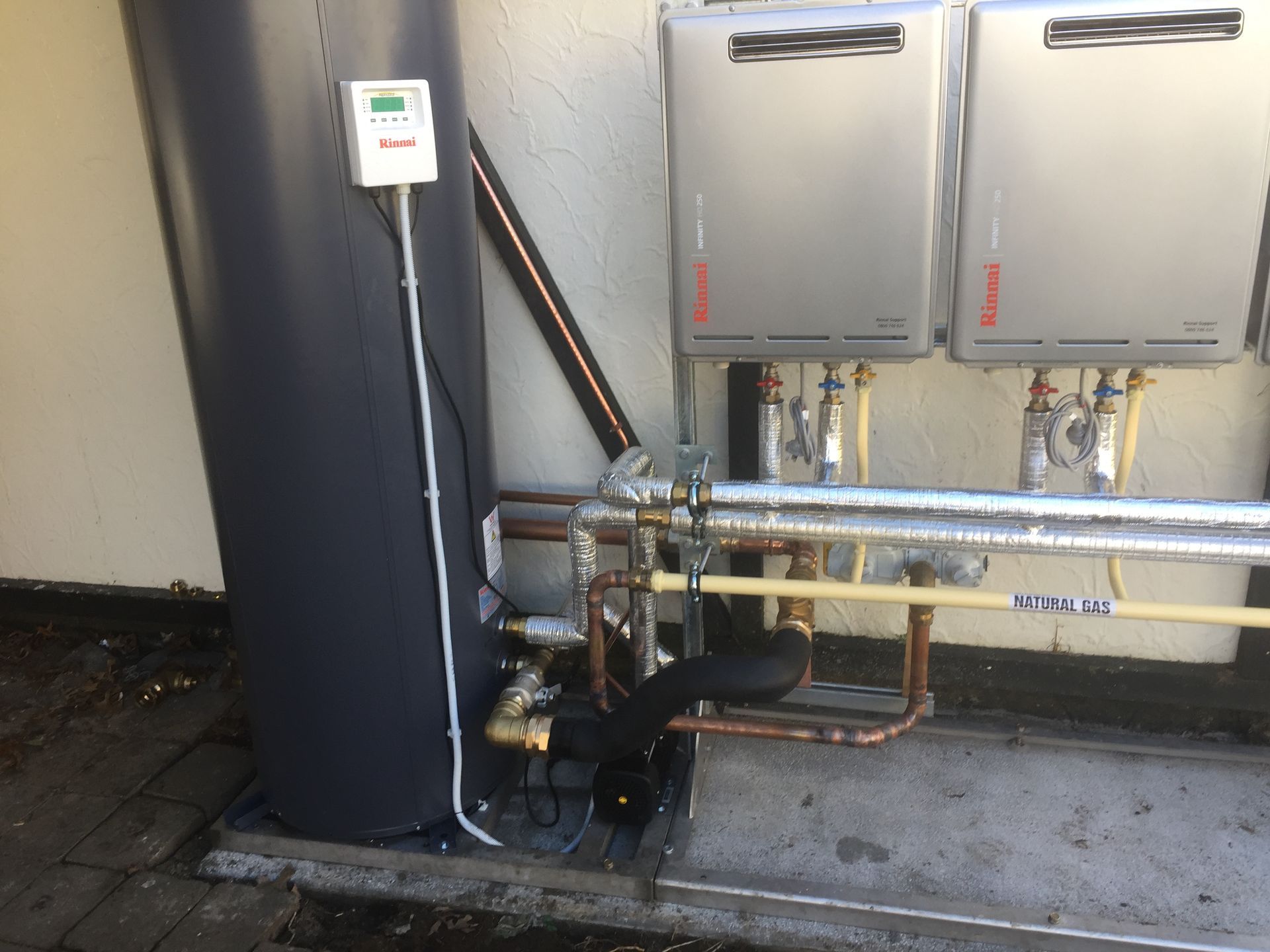 Hands using pliers to tighten a brass fitting on plumbing pipes, set against a yellow wall.