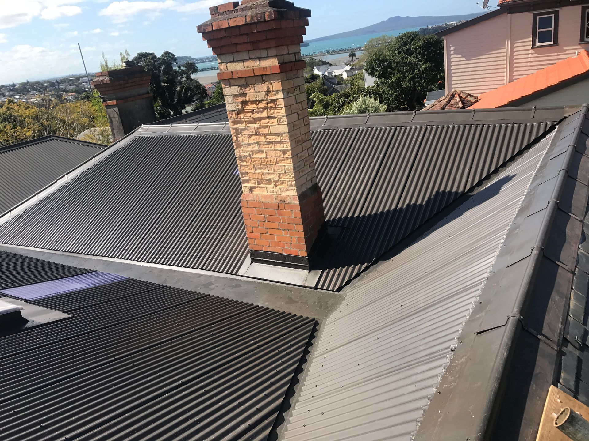 Two people rolling out roofing material on a roof, applying a dark sealant.