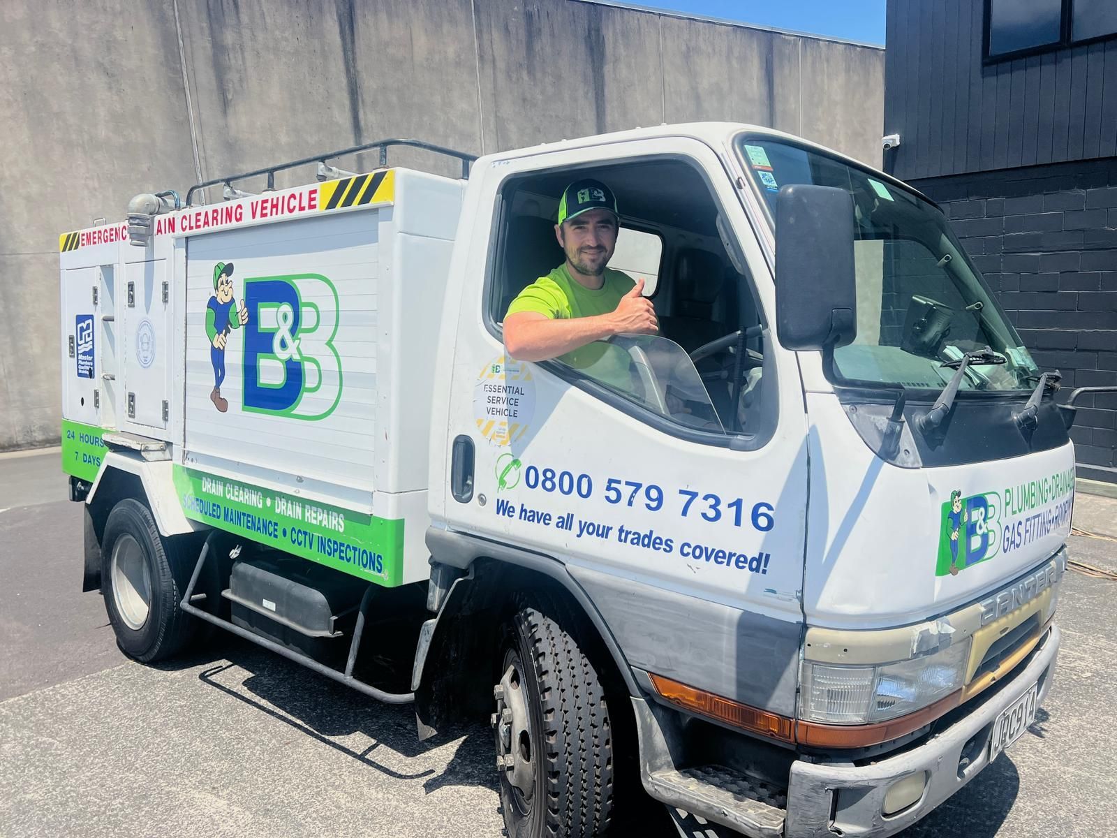 Man in a truck, smiling, giving a thumbs up. The truck is white and green with company branding.