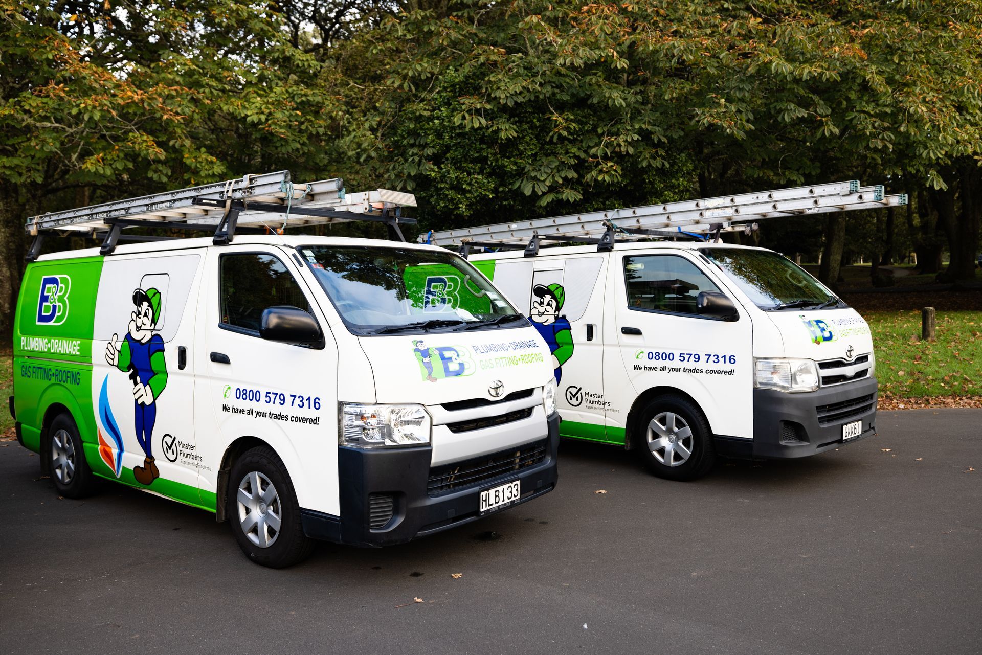 Two white work vans with green and blue logos parked on asphalt.