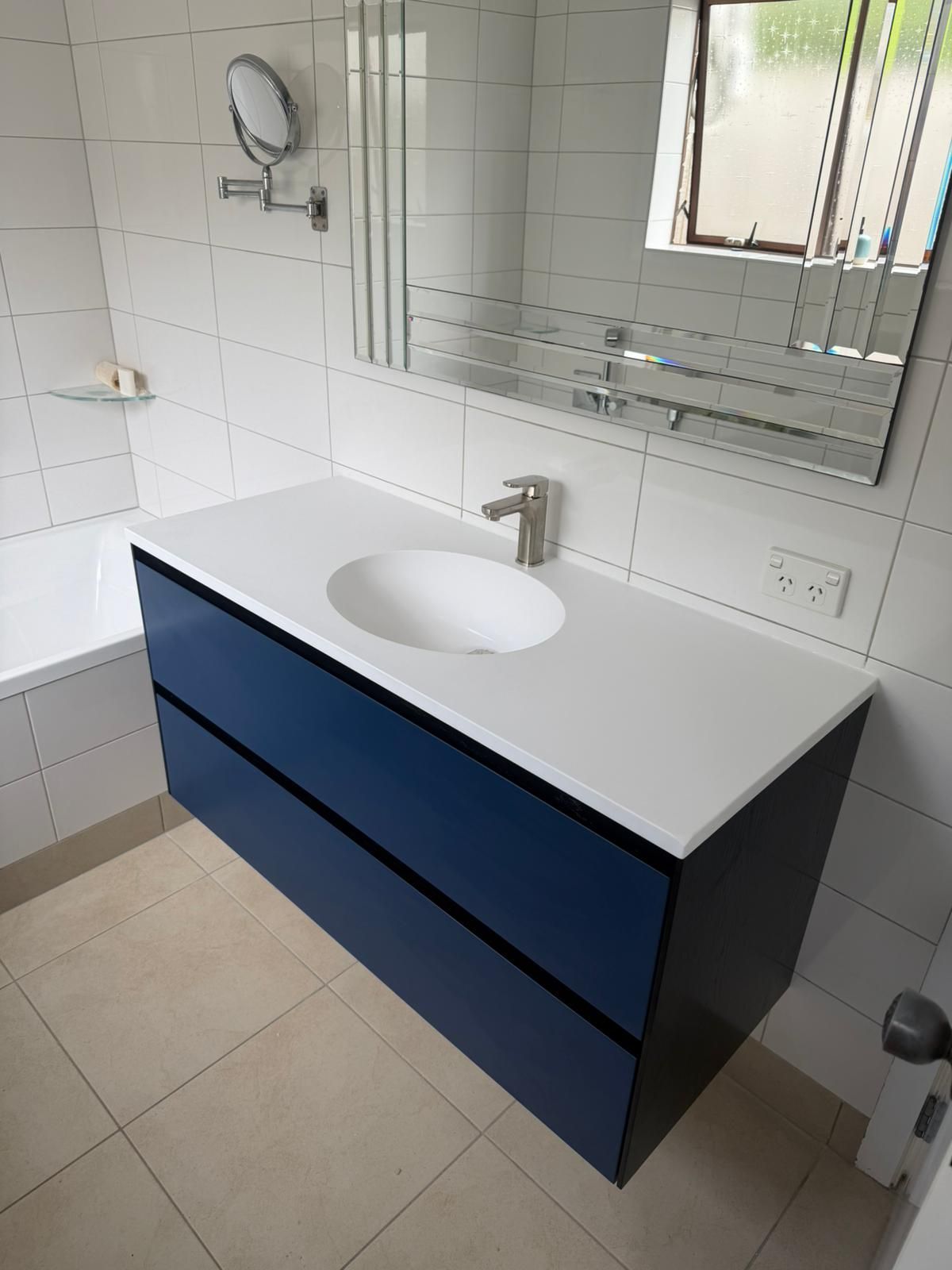 Blue vanity with white countertop and sink in a modern bathroom with white tile walls and a mirror.