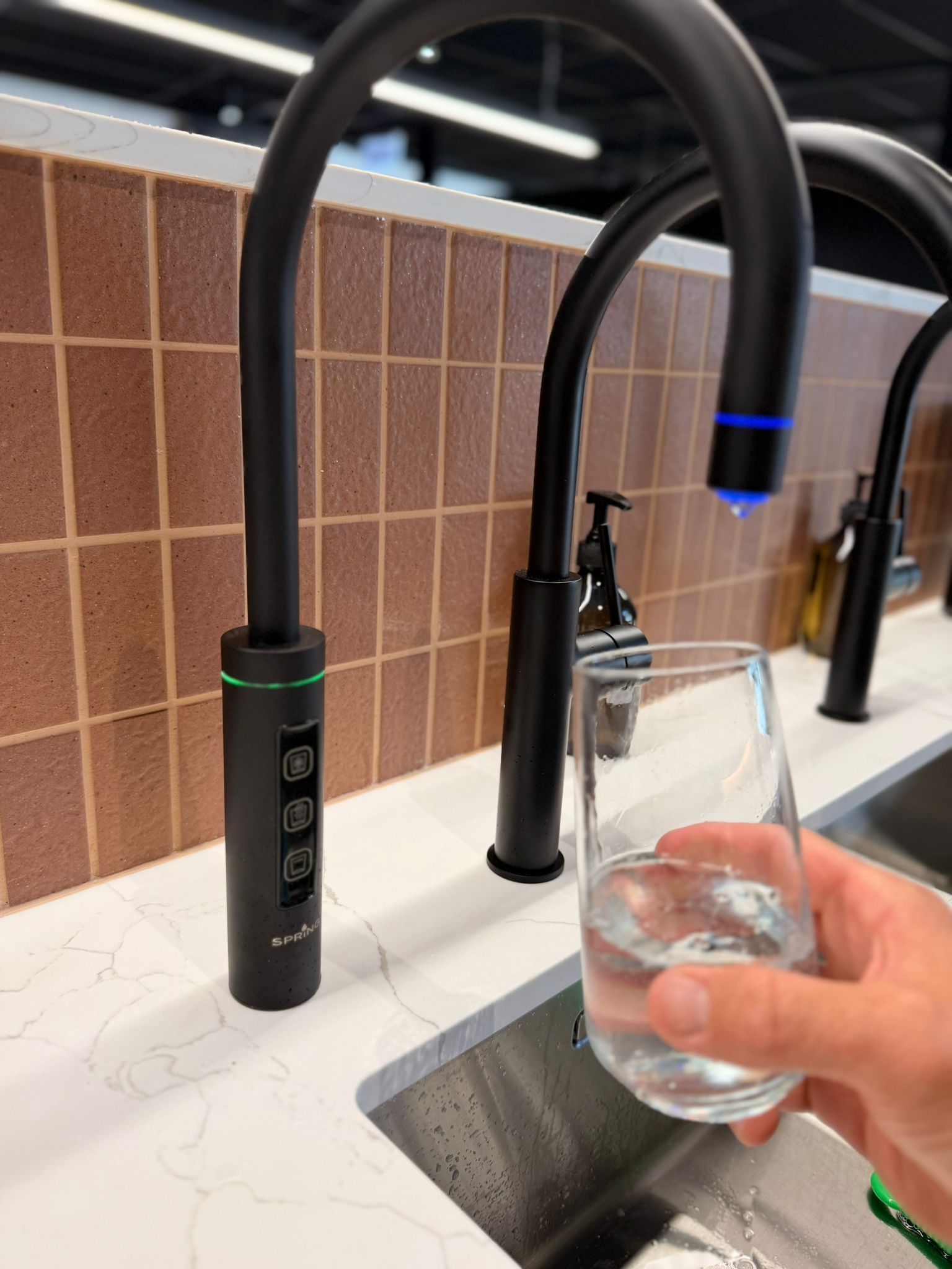 Black kitchen faucet dispensing water into a glass, next to a sink.