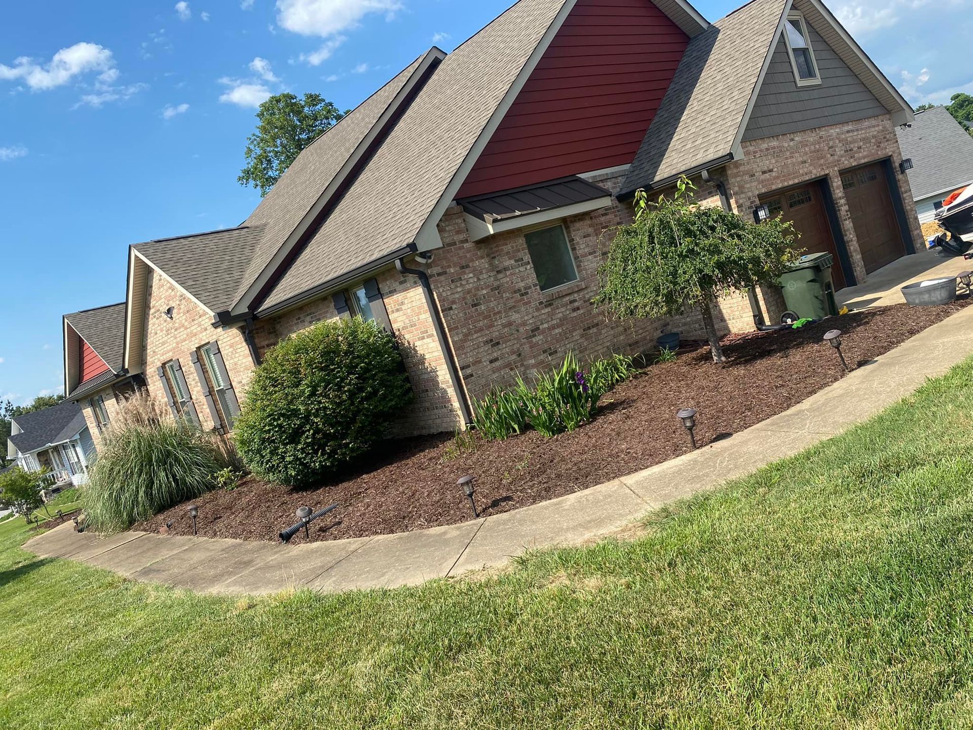A large brick house with a red roof is sitting on top of a lush green hillside.