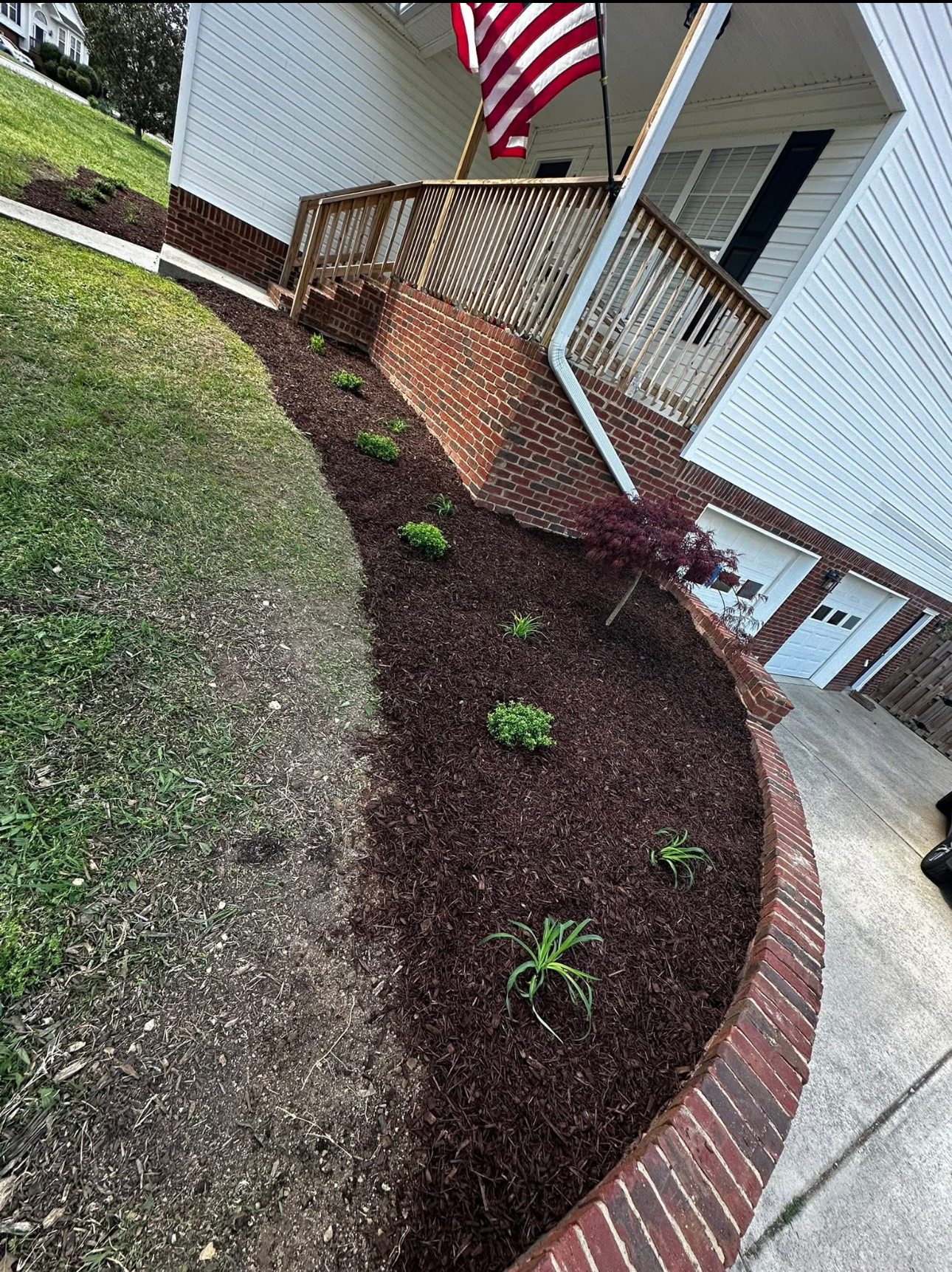 A brick walkway leading to a house with a flag on the porch.