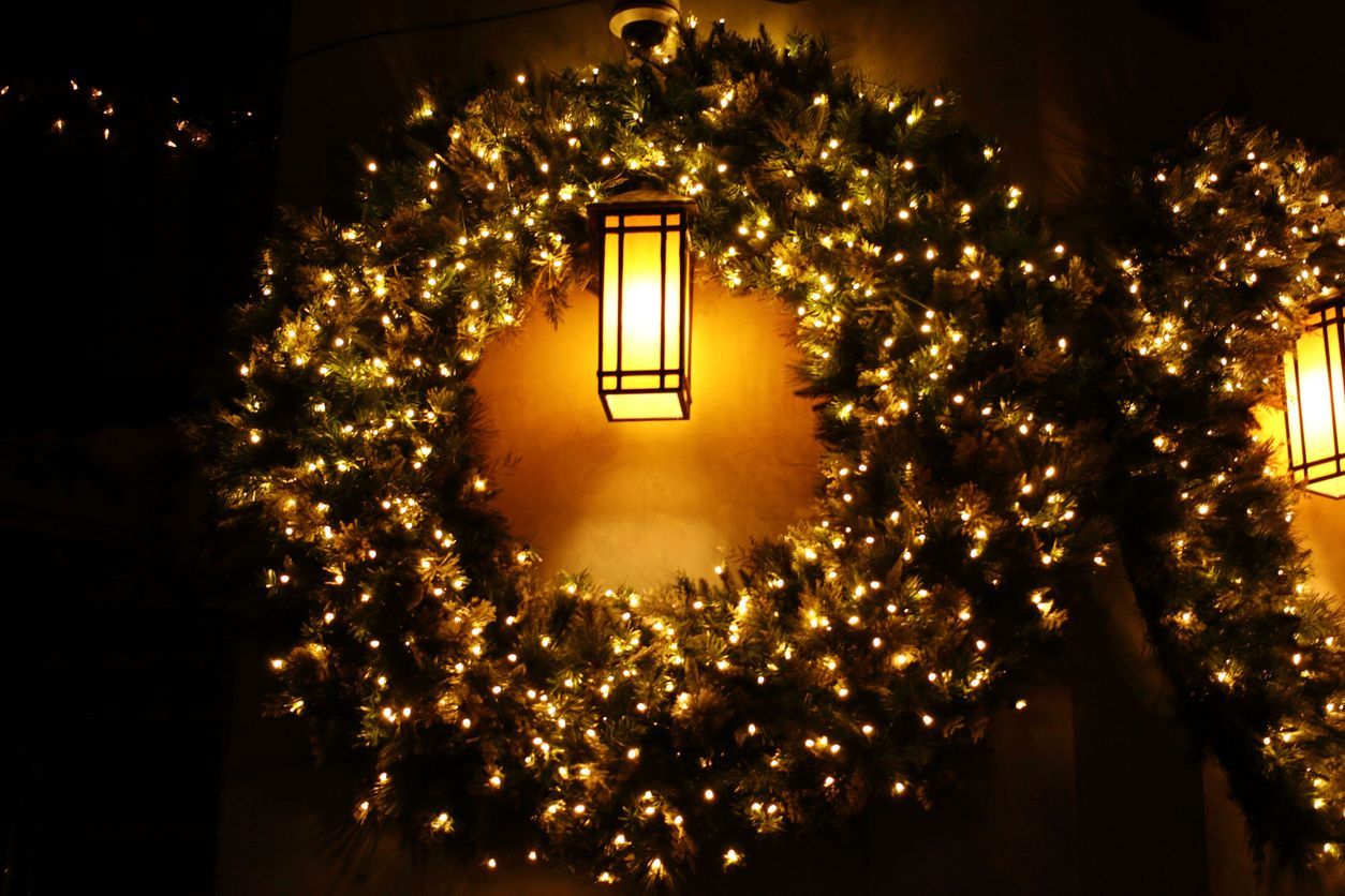Christmas wreath with warm lights around a rectangular lantern hanging on a dark wall.