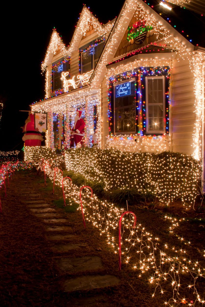 House covered in bright Christmas lights, pathway lined with lights, Santa figure on the porch.