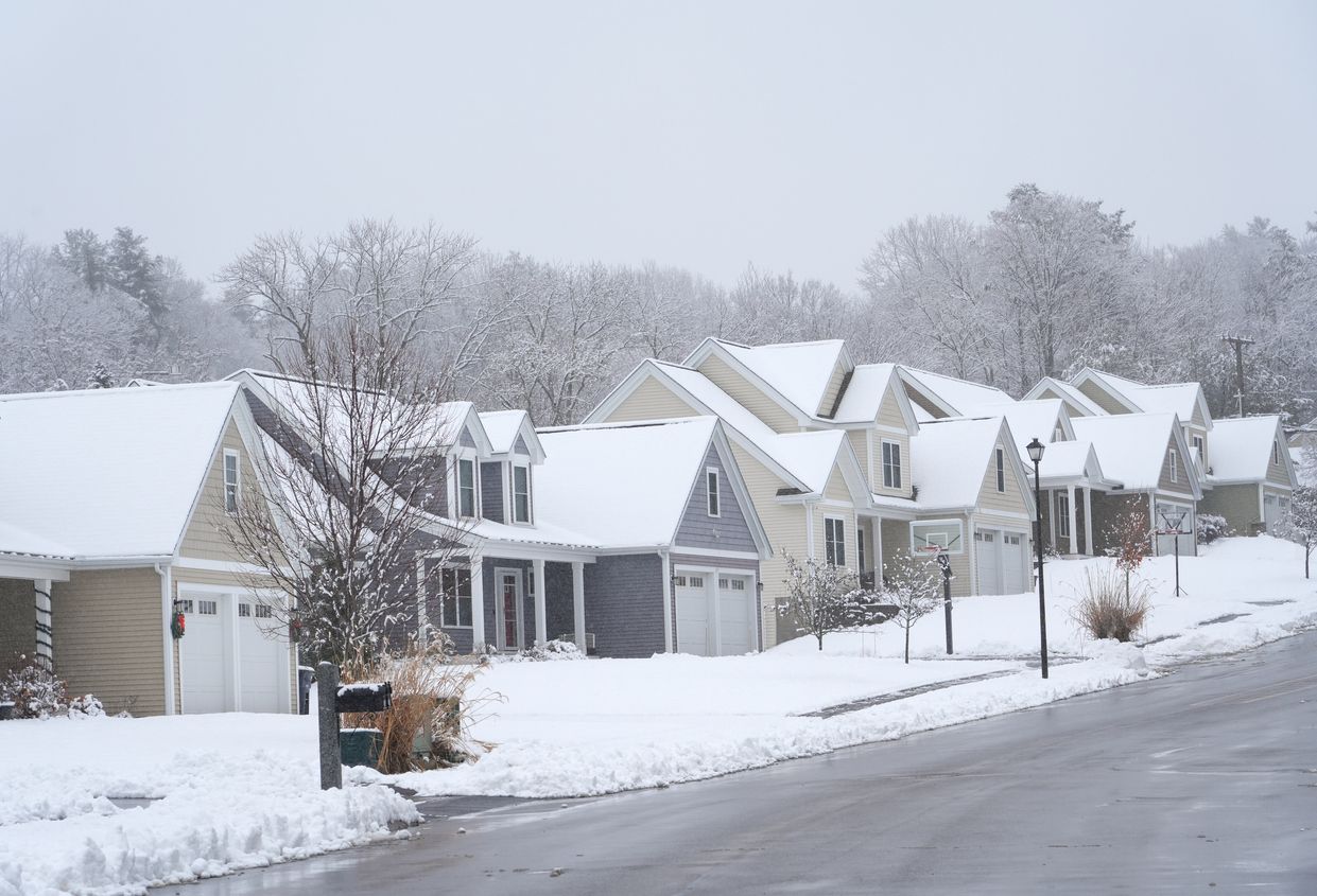 Row of snow-covered houses along a street, trees in the background, winter scene.