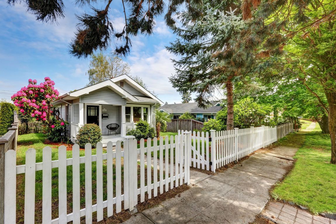 A white picket fence surrounds a small white house.