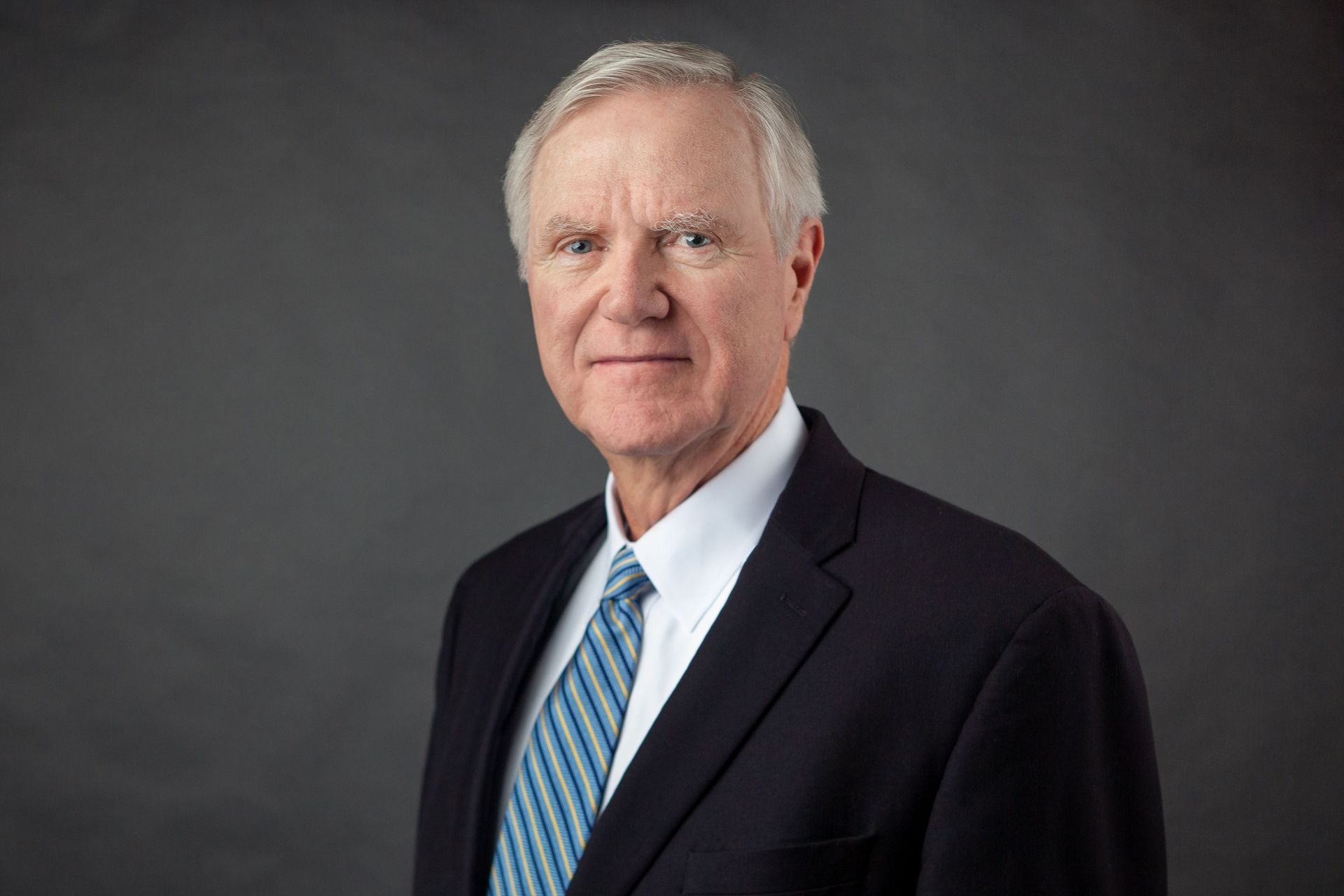 A man in a suit and tie is standing in front of a gray background.