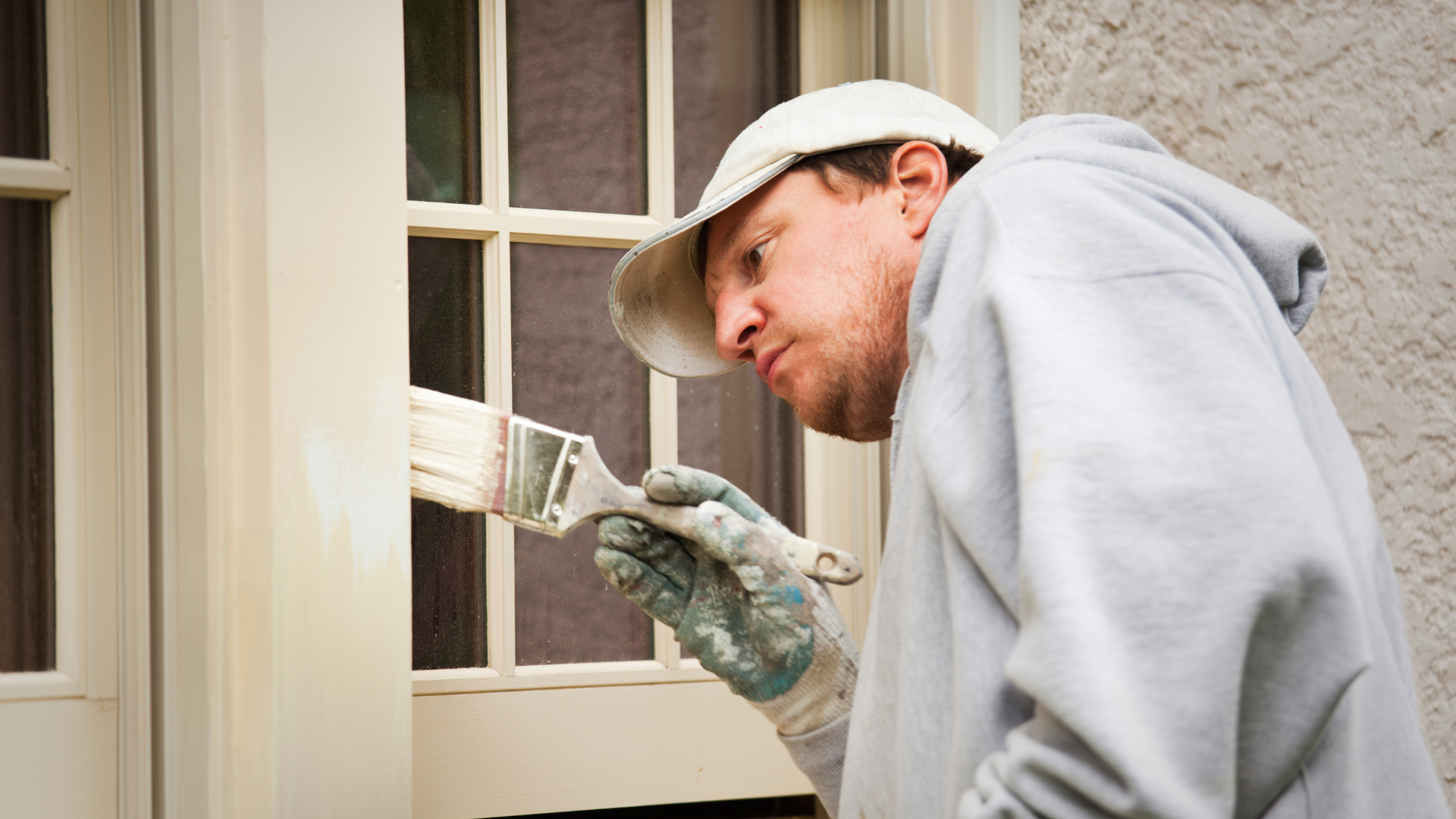 A person is spray painting a white railing on a balcony.