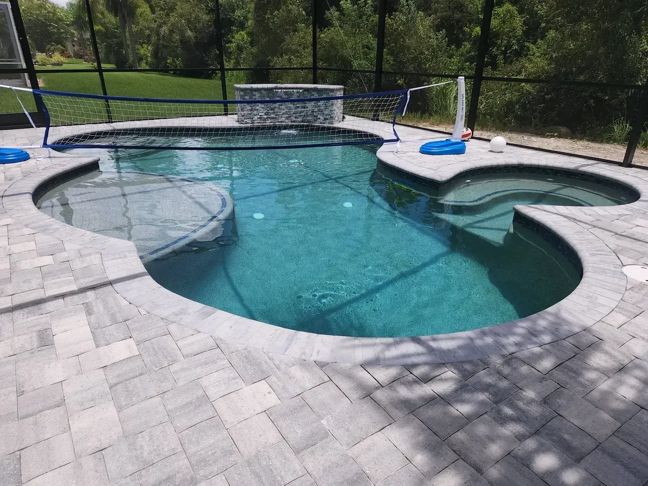 Swimming pool with attached spa and gray paver patio surrounded by a screen enclosure.
