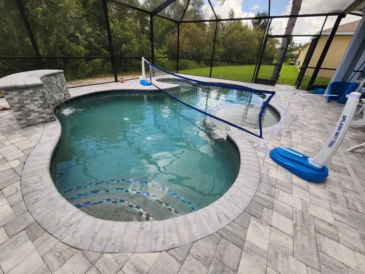 Swimming pool with a volleyball net, surrounded by gray pavers.