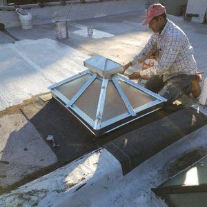 A man is working on a skylight on the roof of a building.