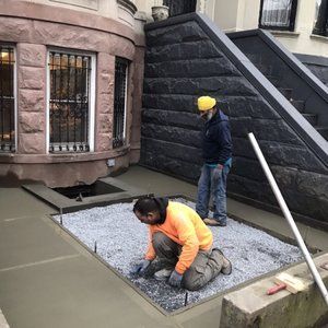 Two men are working on a concrete sidewalk in front of a building.