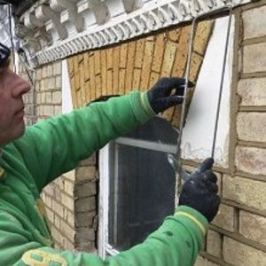 A man in a green jacket is working on a brick wall.