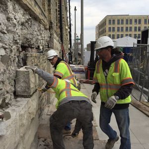 A group of construction workers are working on a stone wall.