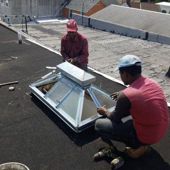 Two men are working on a skylight on a roof