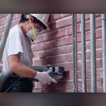 A man wearing a hard hat and mask is working on a brick wall.