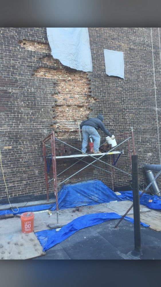 Two men are working on a brick wall on scaffolding.