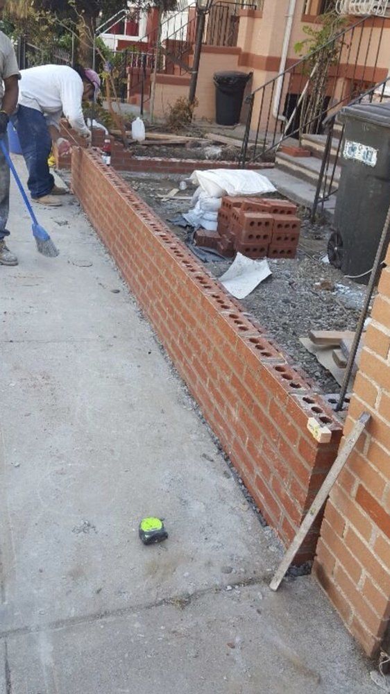 A man is working on a brick wall on the sidewalk.