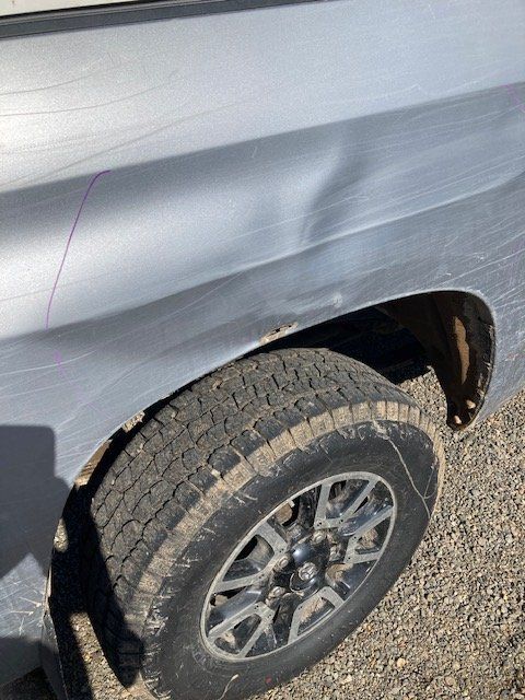 A close up of a truck 's fender and tire on a gravel road.