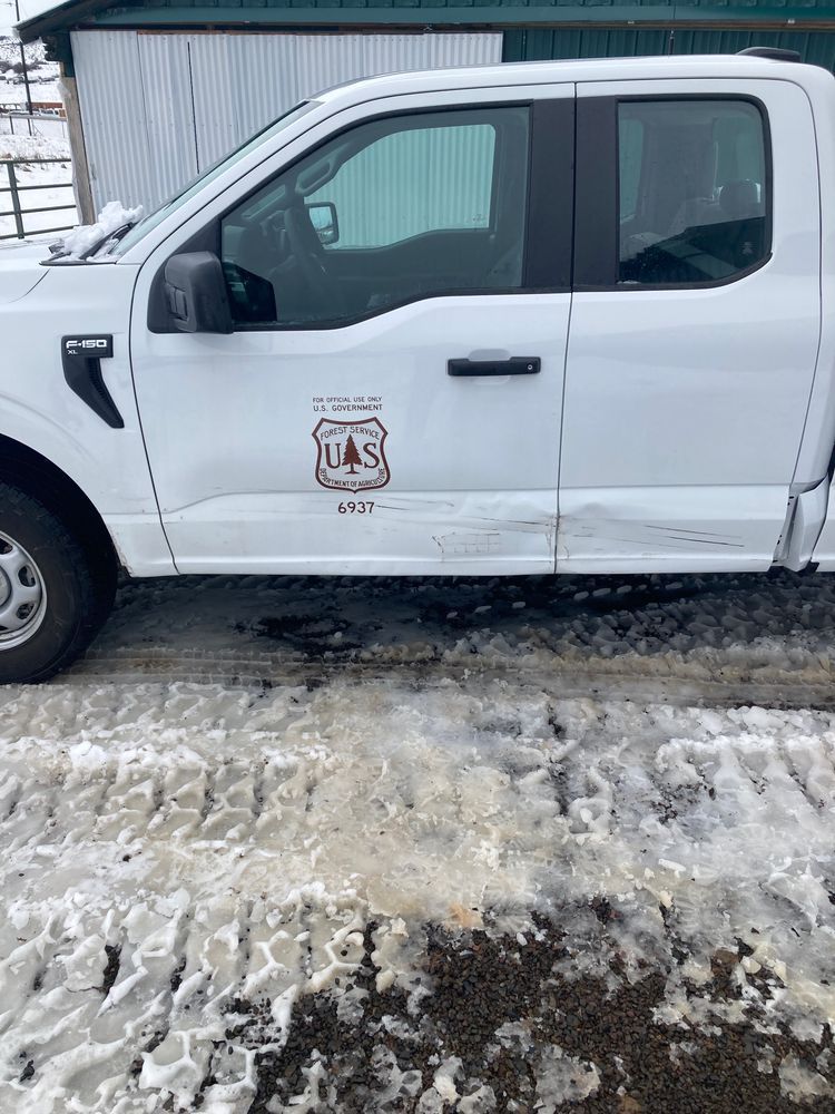 A white truck is parked in the snow in front of a shed.