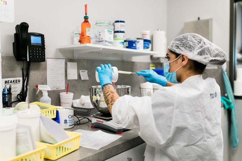 A woman wearing a mask and gloves is working in a lab.