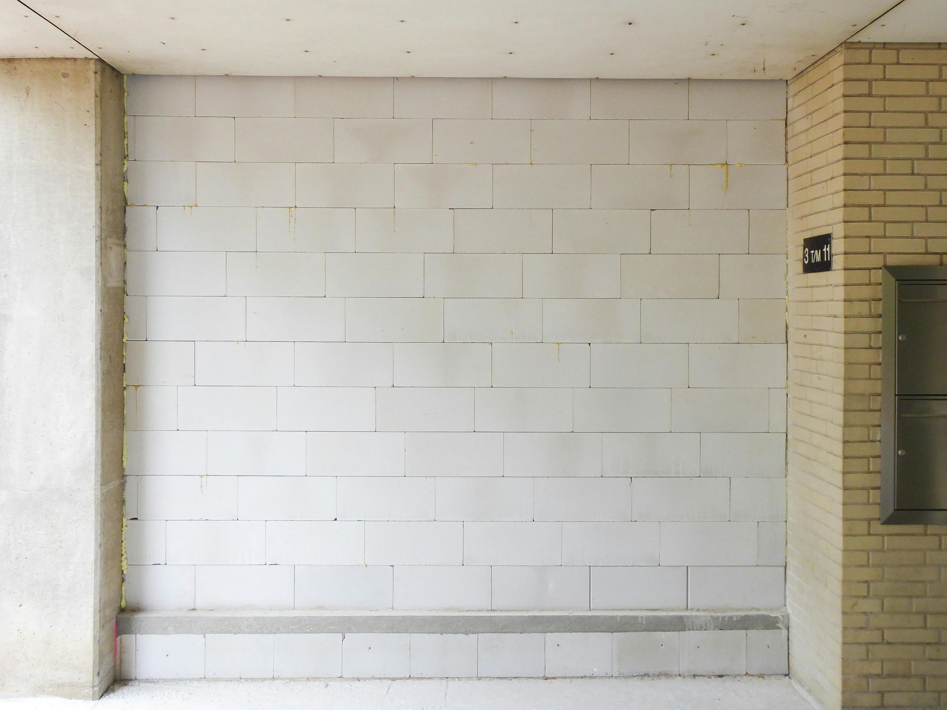 Empty white block wall in a building corridor beside a brick column and doorway