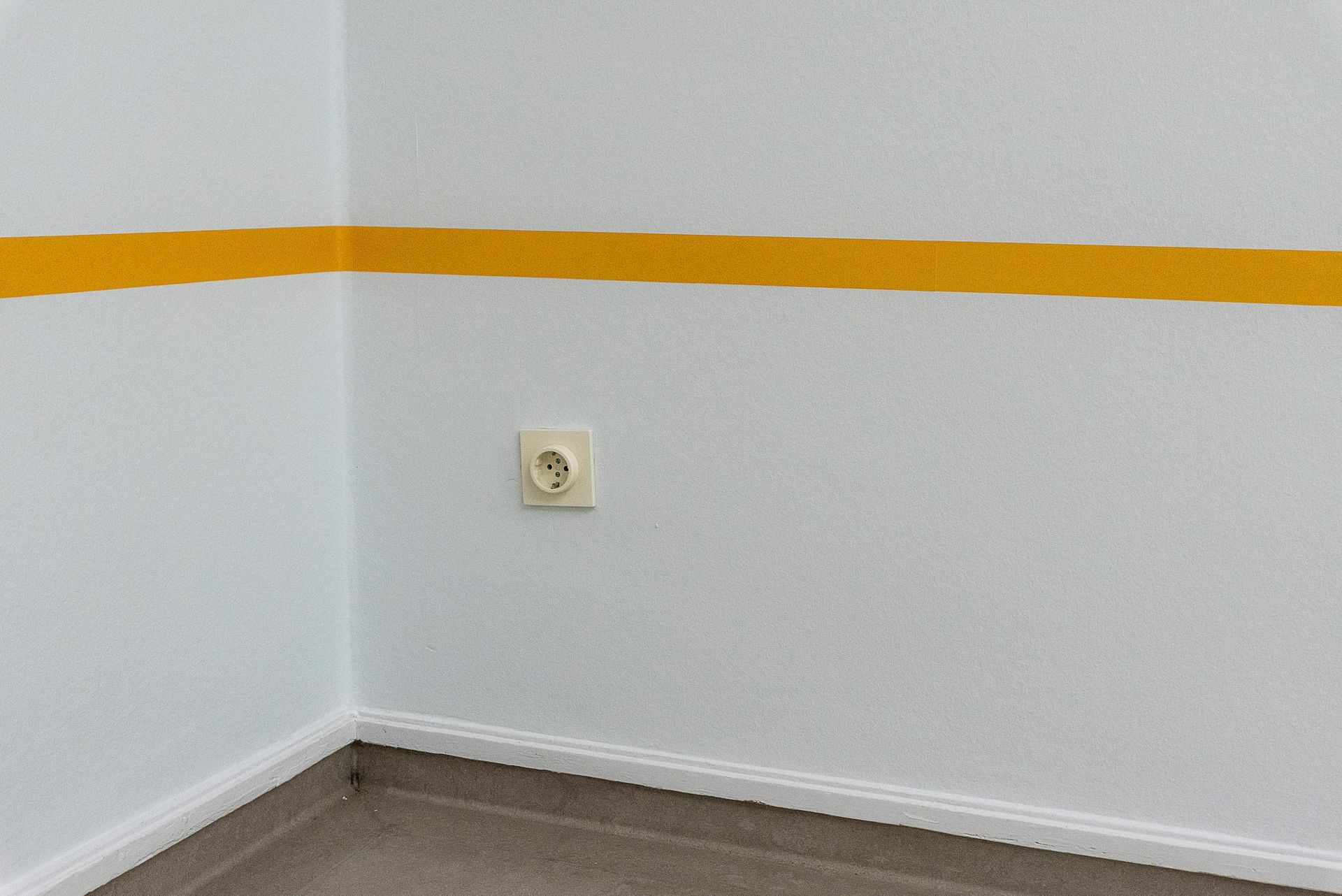 Empty white corner with orange stripe and wall outlet above wood floor